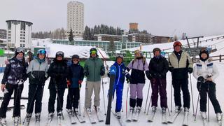 10 skiers lined up in a row. The sixth skier is the instructor Luca, who has his right ski raised.