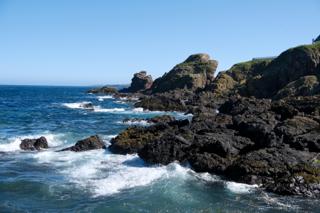 A rugged coastline with jagged rocks dotting its shore under a blue sky.