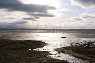 A cloudy sky over a coastal landscape with poles indicating a path across mudflats.