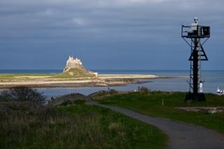 An overcast sky looms above a ruined castle and lighthouse amidst a coastal landscape.