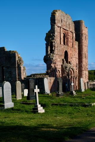 An old stone building with a cross and gravestones under clear skies.