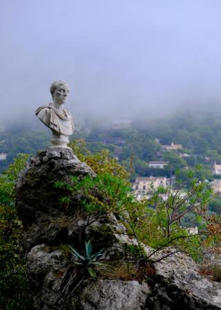 A marble Roman bust on a rock, with misty wooded hills and villas behind.